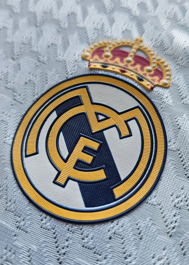 Close-up of Real Madrid CF crest with gold crown and blue RM initials on a white background.