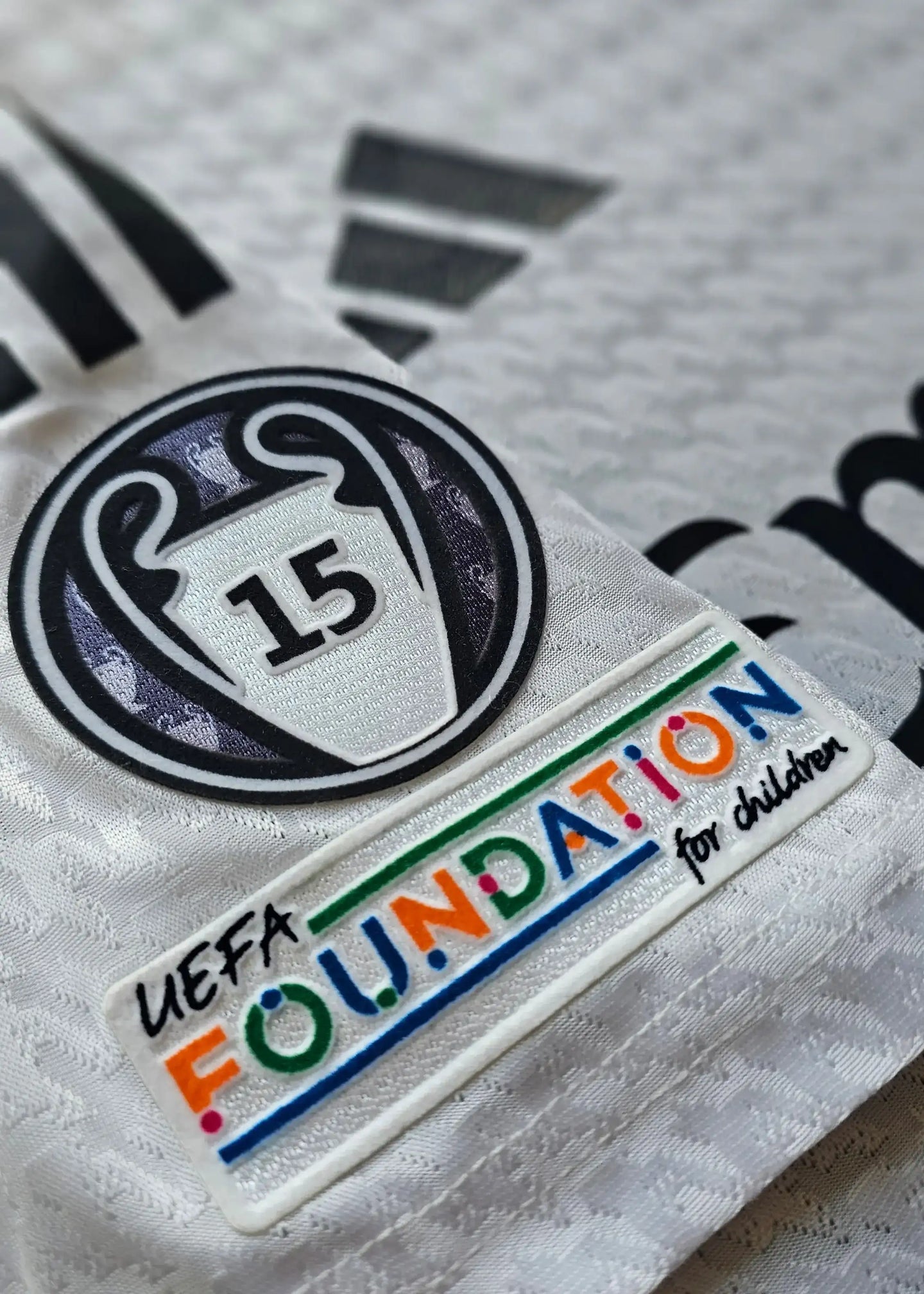 Detail of UEFA Champions League patch with '15' and UEFA Foundation for children label on a white shirt.