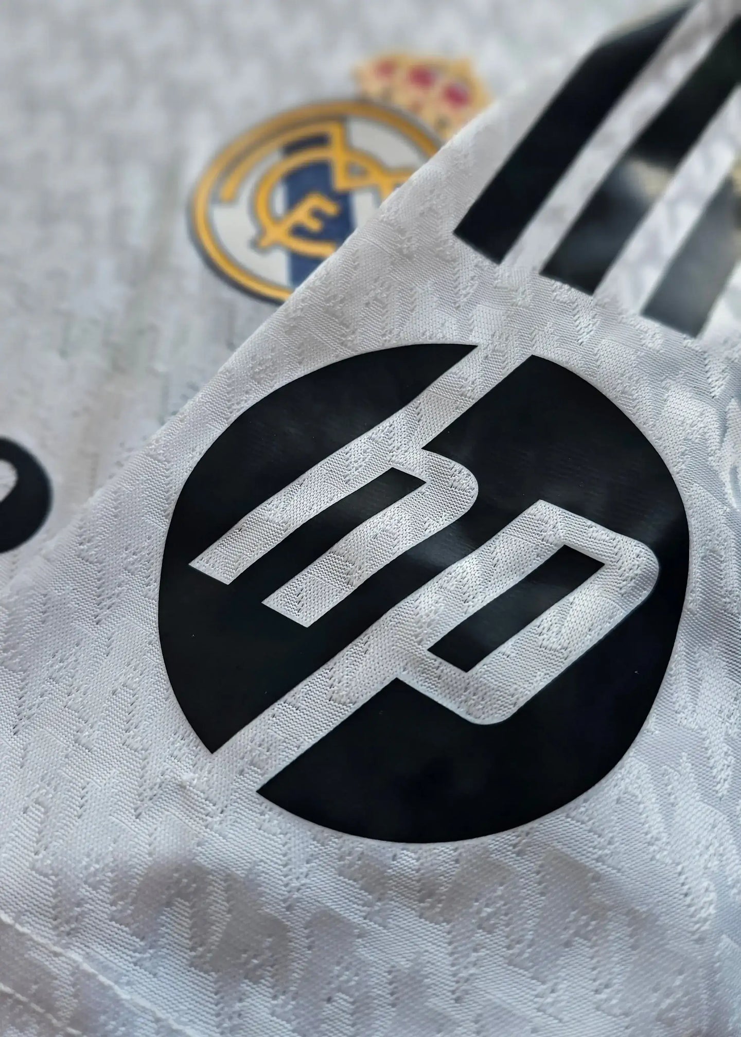 Close-up of Real Madrid crest and black HP logo on a white football shirt.