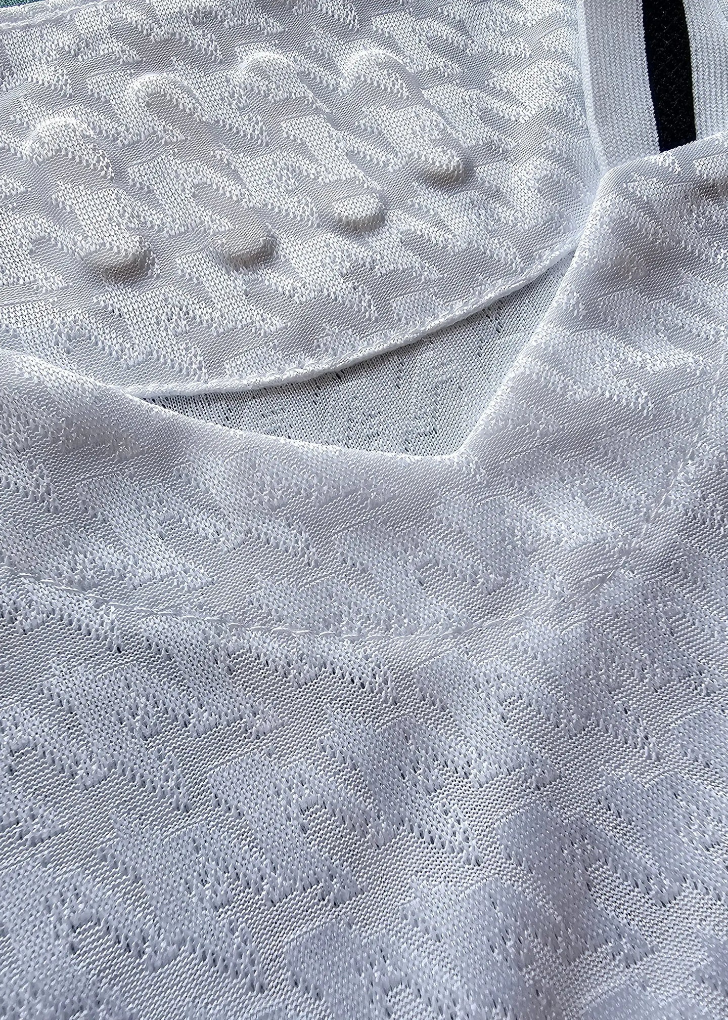 Close-up detail of the textured fabric on the collar and shoulder of a white football shirt.