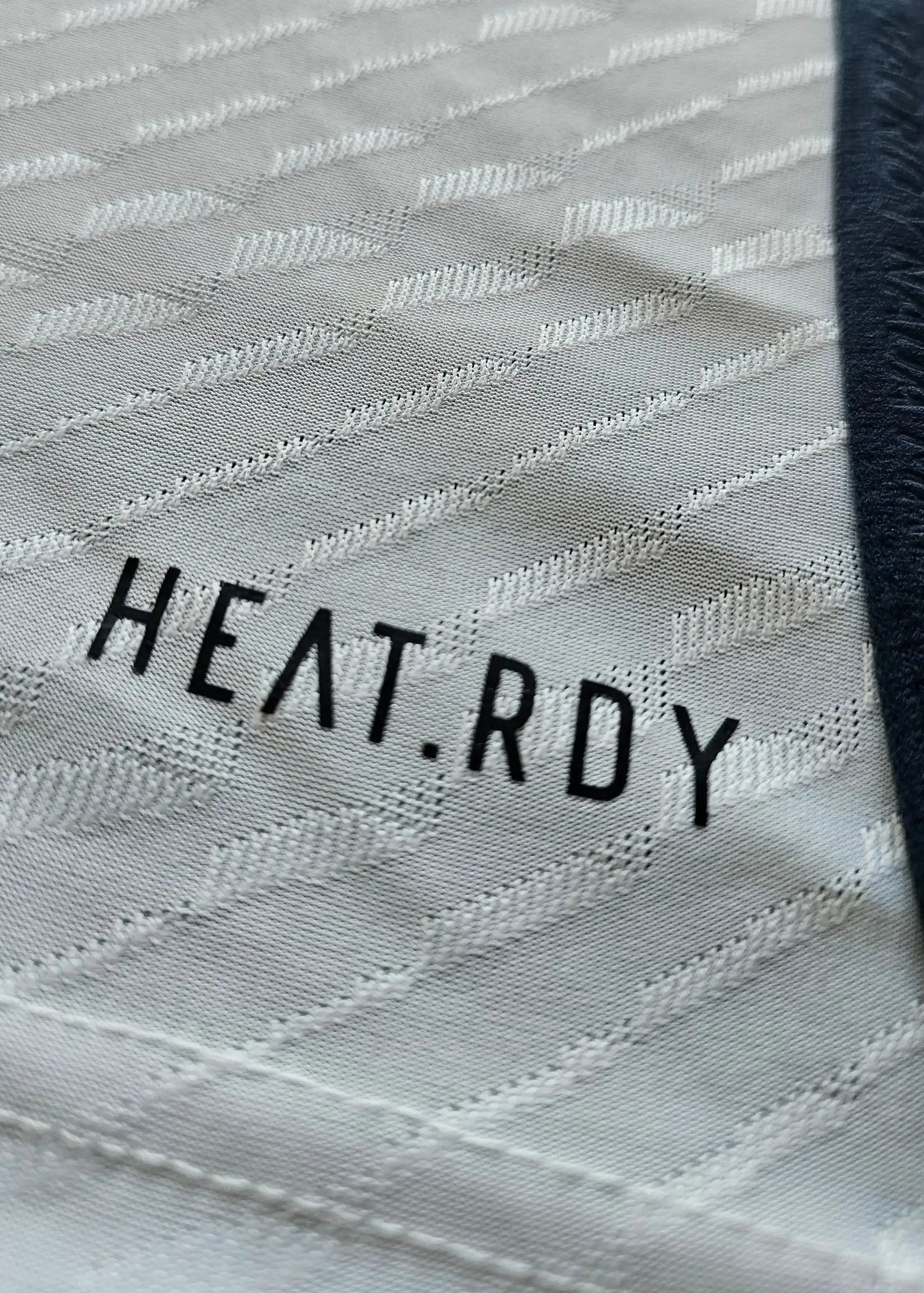 Close-up of the fabric showing the text HEAT.RDY on a white football shirt.