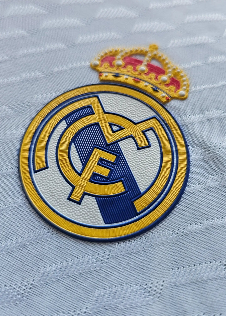 Real Madrid crest with gold crown and blue detailing on a white shirt.