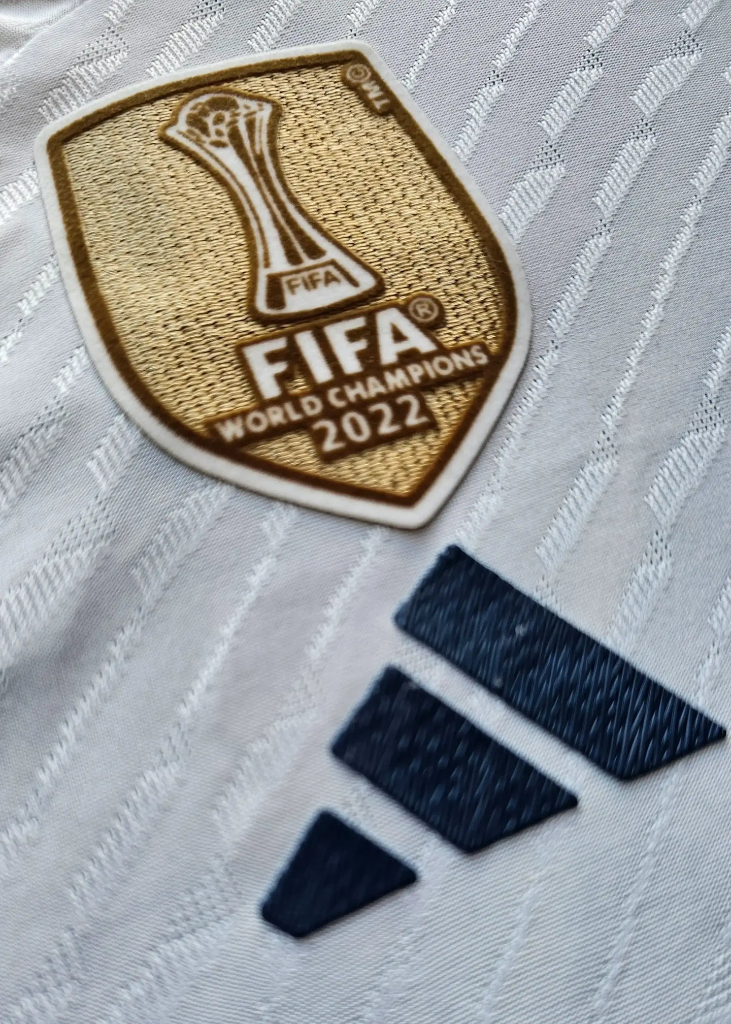 FIFA World Champions 2022 badge in gold with navy adidas logo on a white football shirt.
