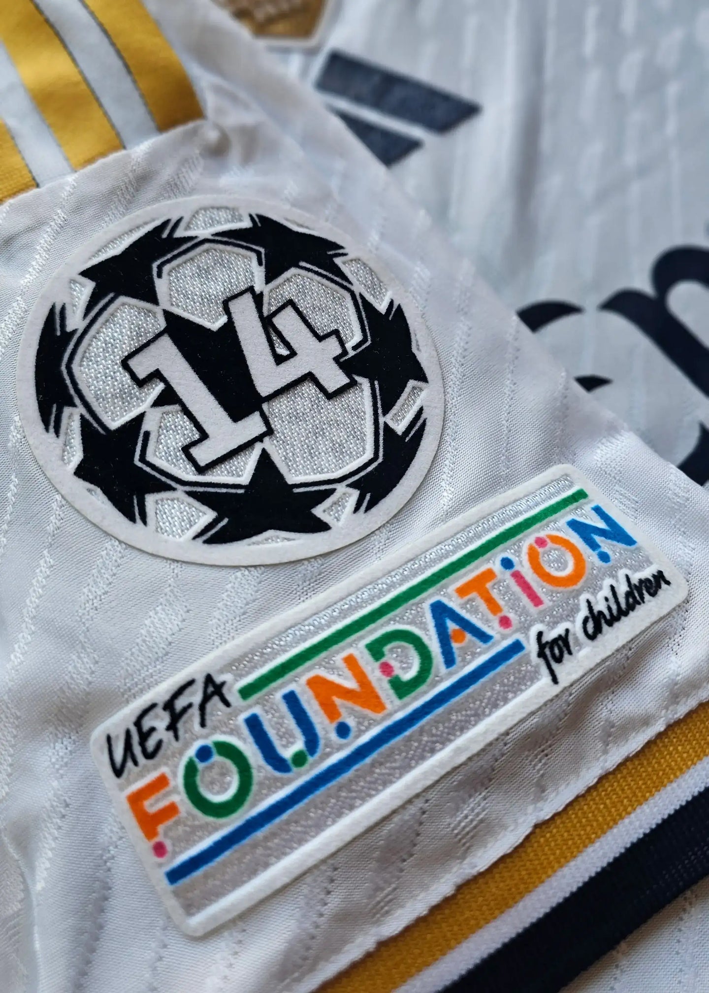 Close-up of a white football shirt featuring UEFA FOUNDATION for children patch and No. 14 badge.