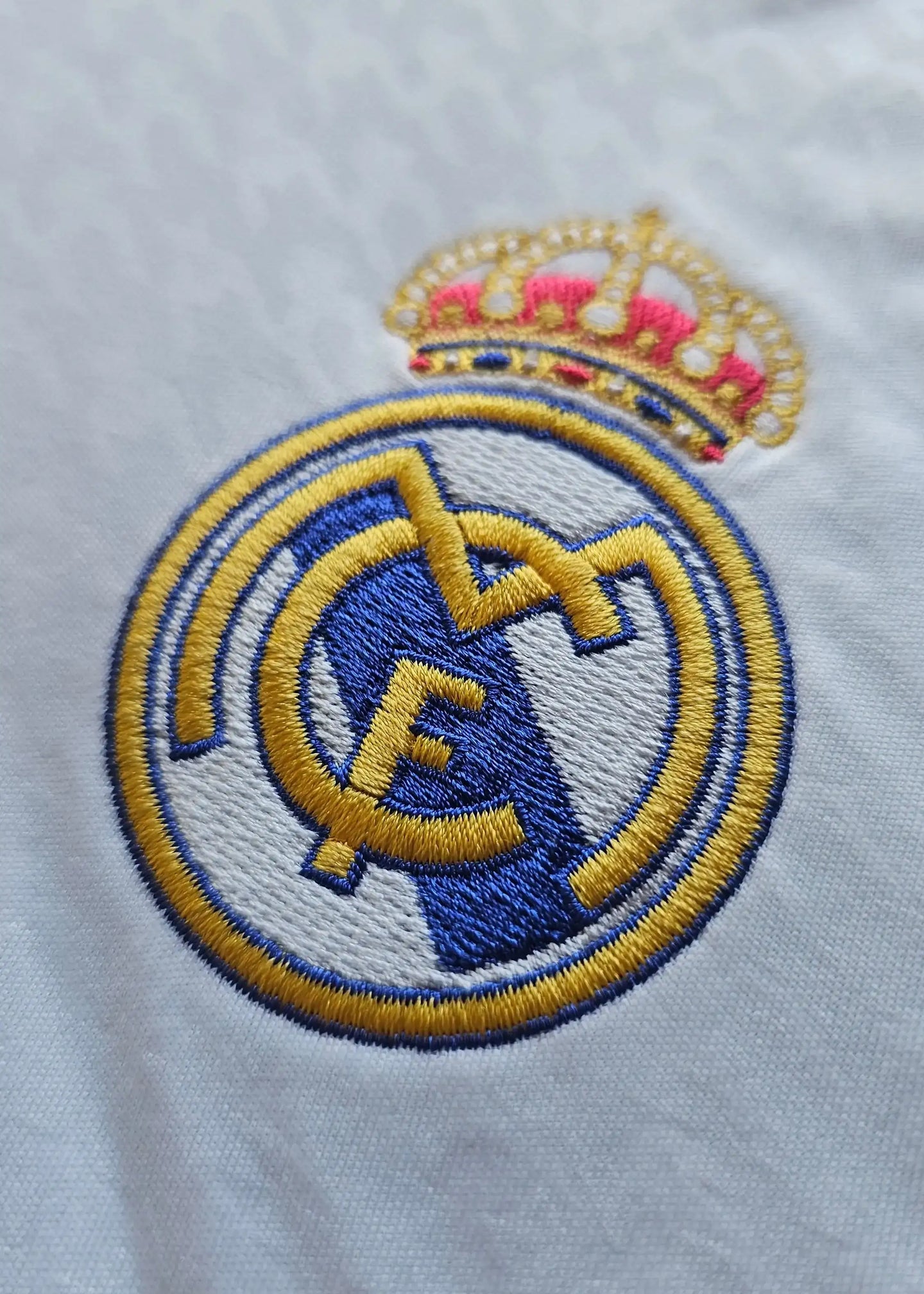 Close-up of the Real Madrid CF crest with a gold crown and blue accents on a white shirt.