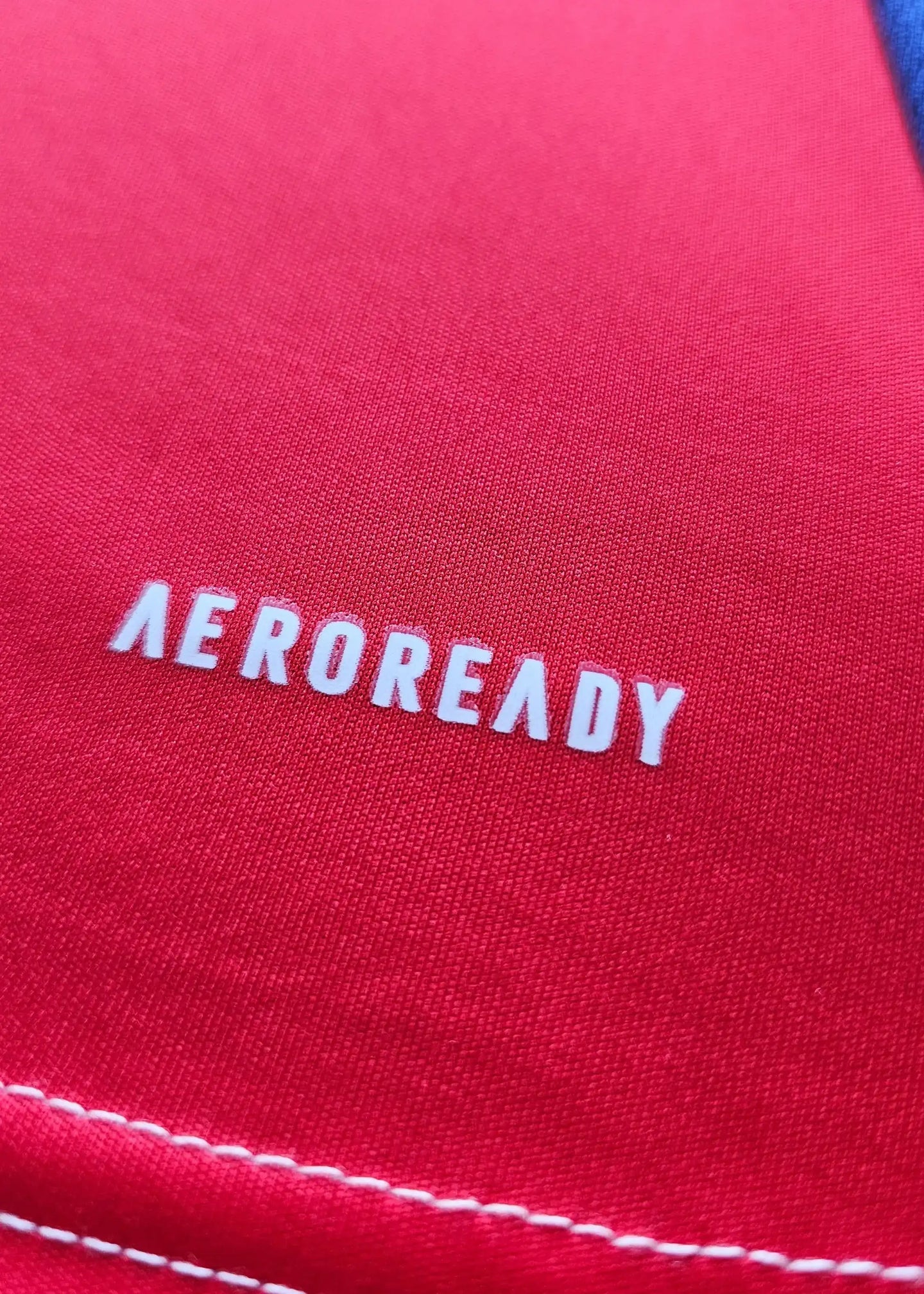 Close-up of red fabric featuring white 'AEROREADY' branding on the shirt.