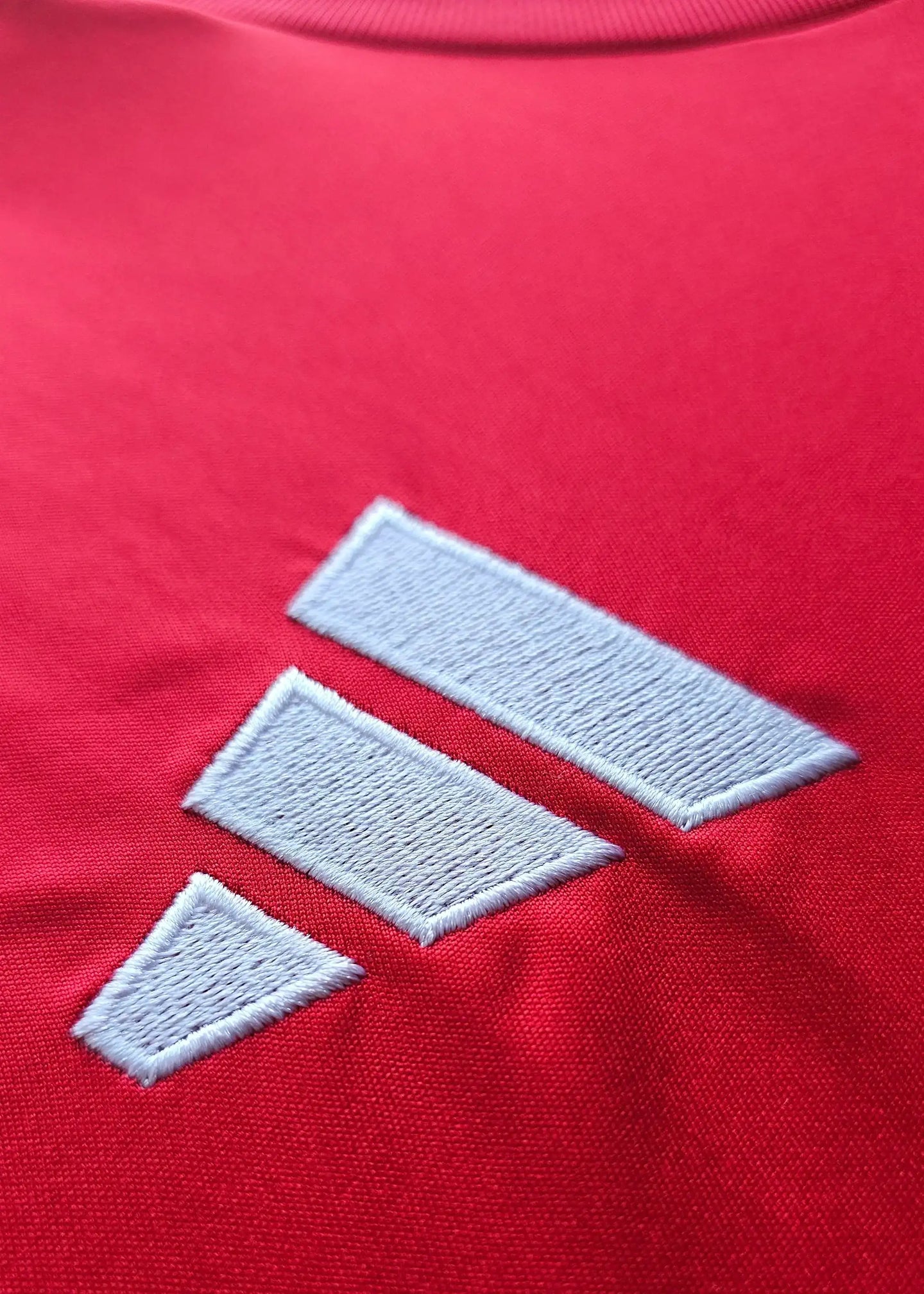 Close-up of white adidas logo on a red Arsenal shirt fabric.