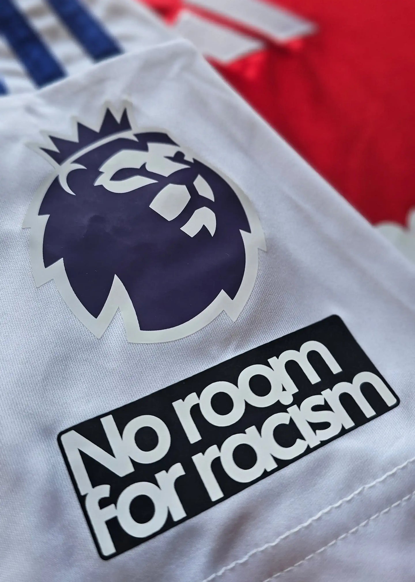 Premier League logo with lion crest and text 'No room for racism' on a white football shirt.