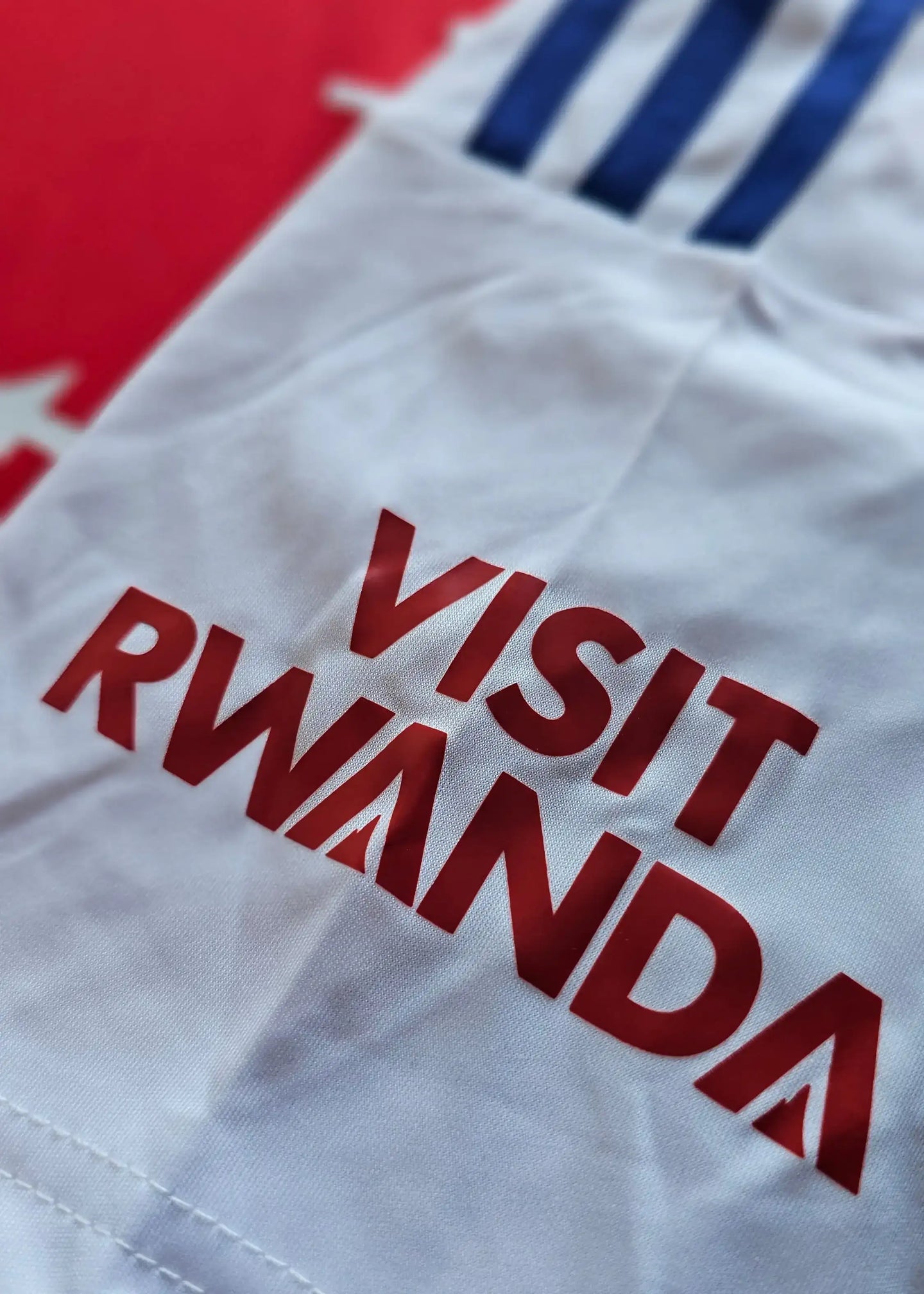 Close-up of white shirt featuring red 'VISIT RWANDA' text and blue stripes.