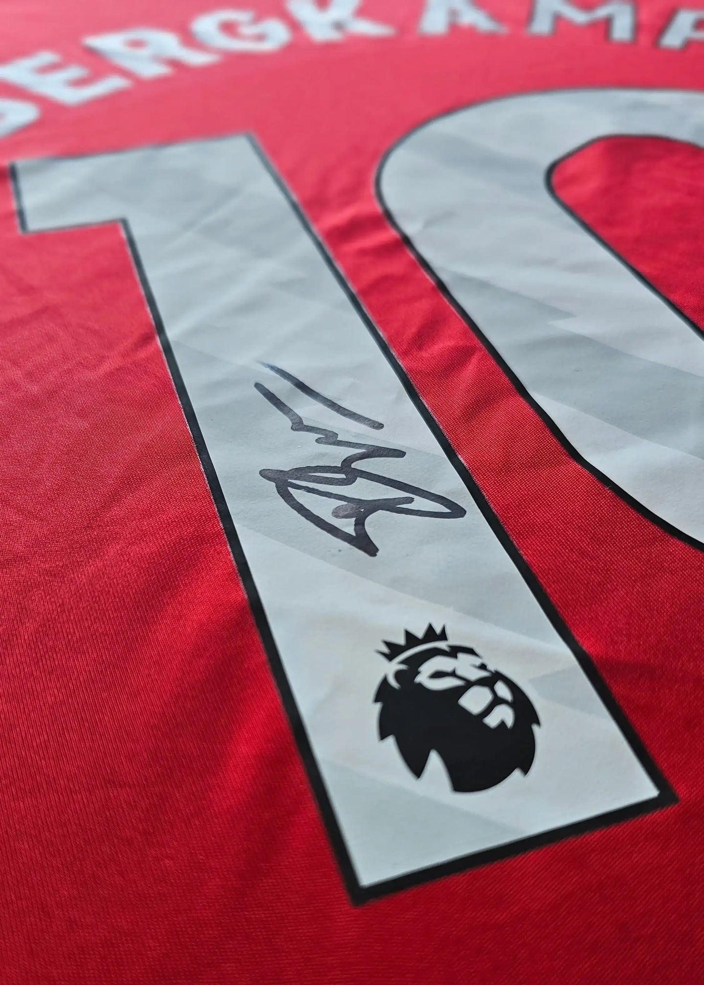 Signature of Dennis Bergkamp on the red Arsenal shirt, featuring No. 10 and Premier League badge.
