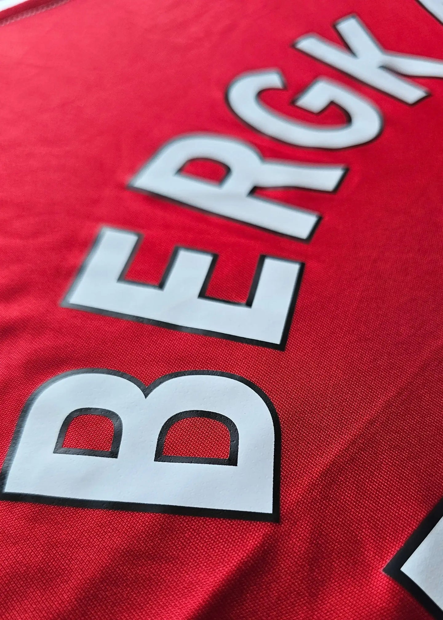 Close-up showing the name BERGKAMP in large white letters on a red Arsenal shirt.