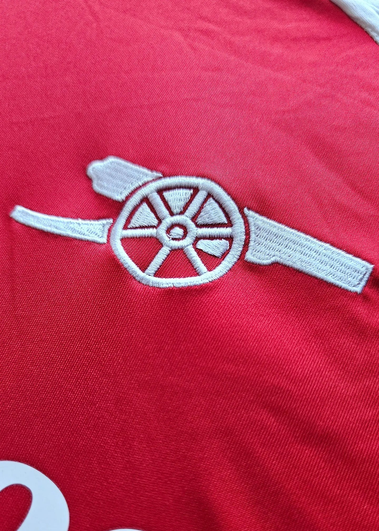 Embroidered Arsenal cannon crest in white on a red football shirt.