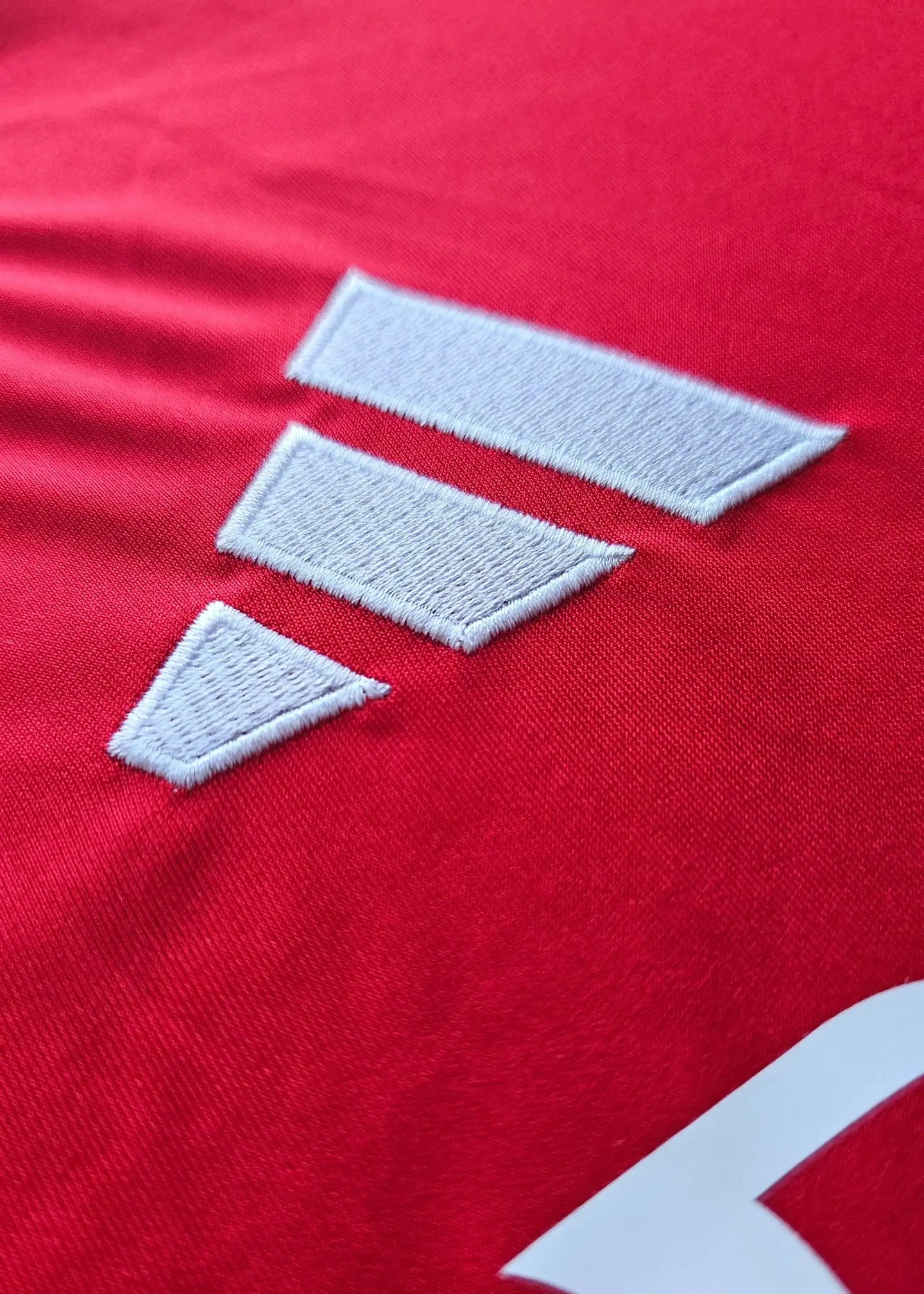 Close-up of three white embroidered stripes on a red Arsenal football shirt.