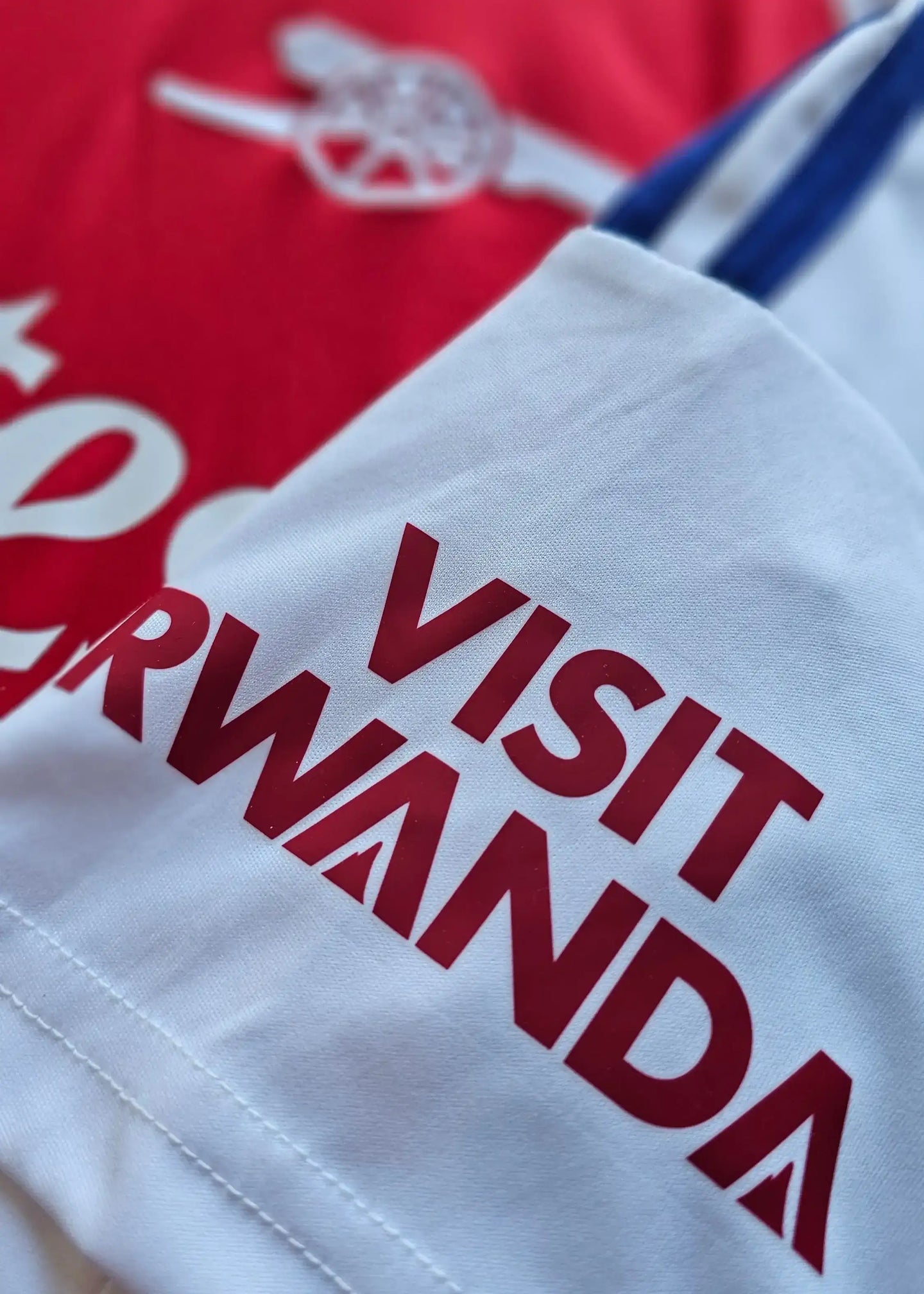 Close-up showing white shirt with 'VISIT RWANDA' in red text and Arsenal crest partially visible.