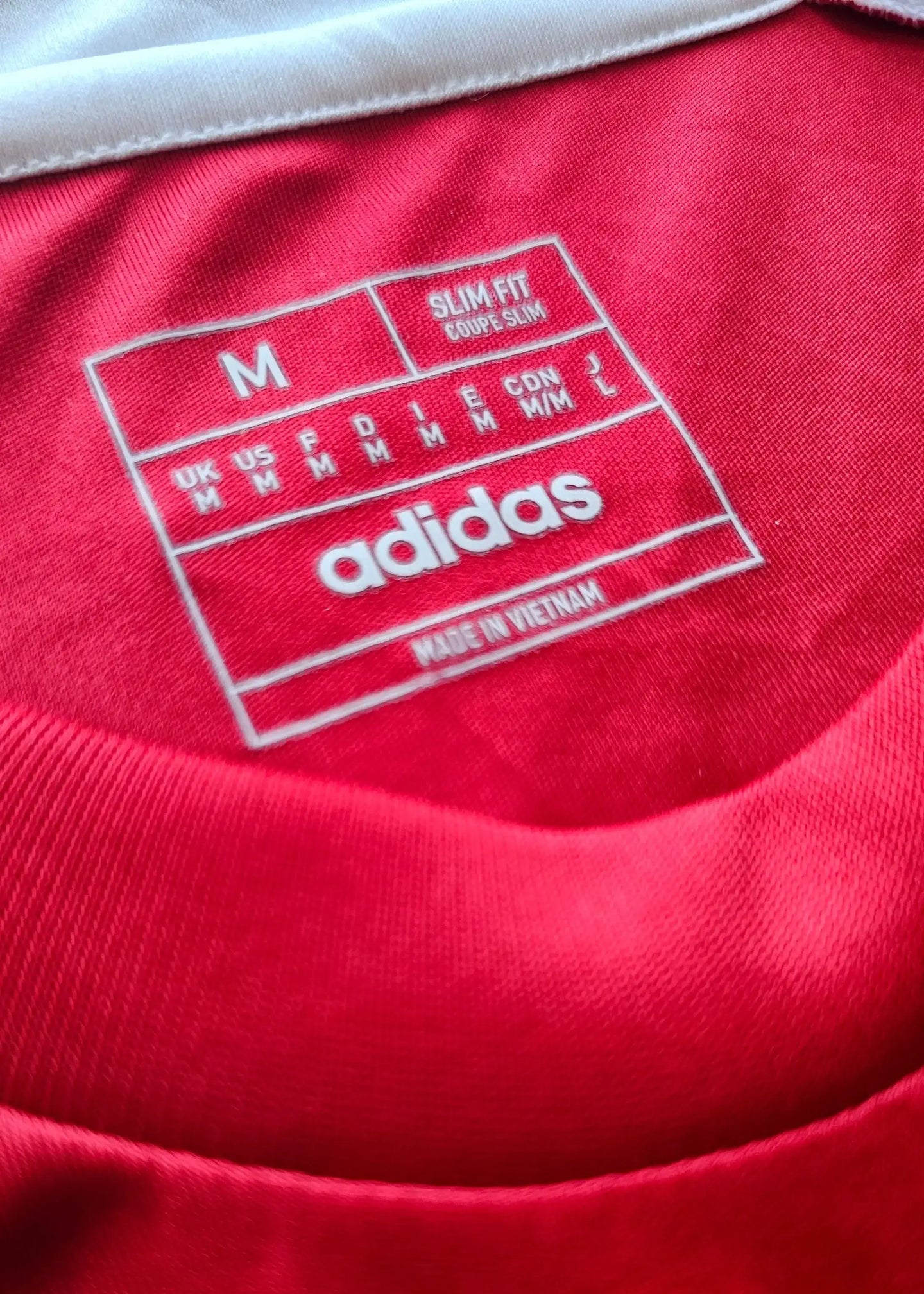 Size M slim fit label inside a red adidas football shirt with white trim.