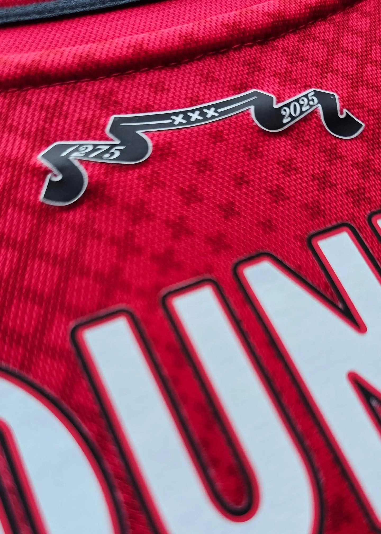 Crest detail showing '375' and '2025' on a red football shirt with intricate texture.