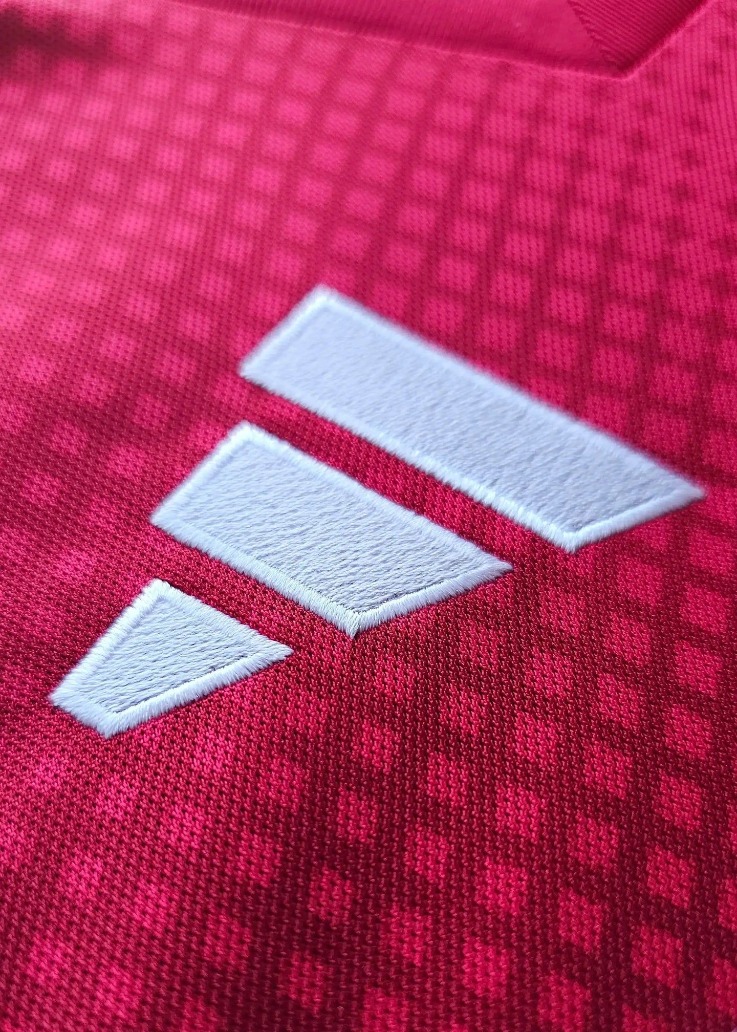 Close-up of the white adidas logo on a red textured fabric shirt.
