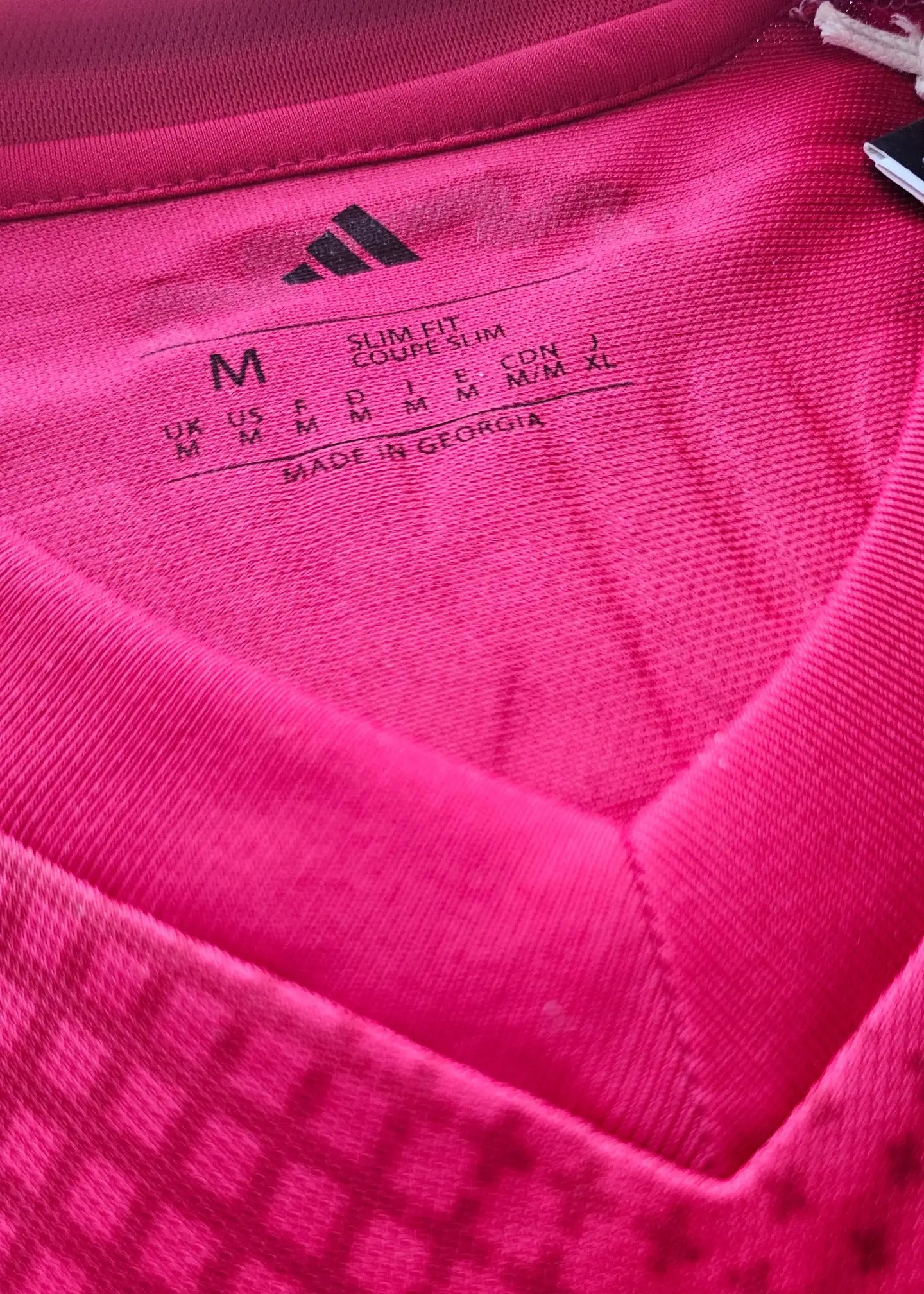 Size M adidas tag showing slim fit details and care instructions on the red shirt.
