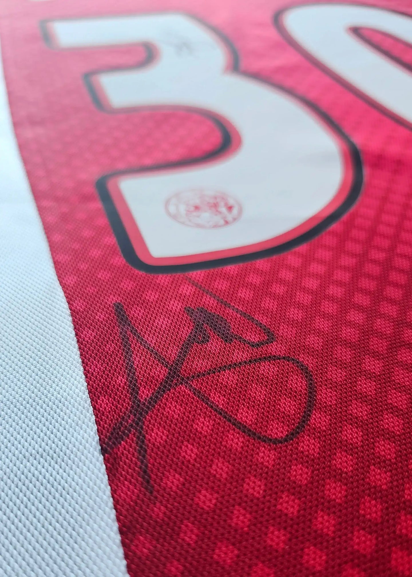 Detail of Aaron Bouwman 30 Ajax shirt featuring a signature on a red background.