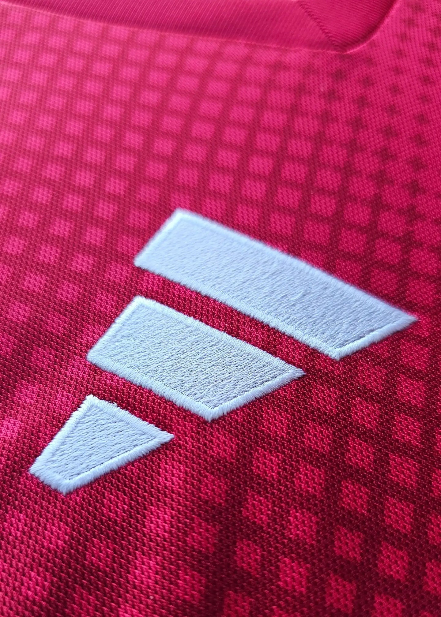 Close-up of a white brand logo on the red fabric of the Ajax signed football shirt.