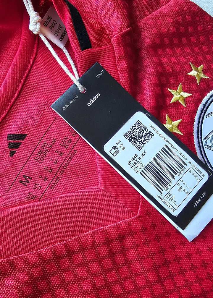 Close-up of the adidas tag showing size 'M', red fabric with three gold stars and black detailing.