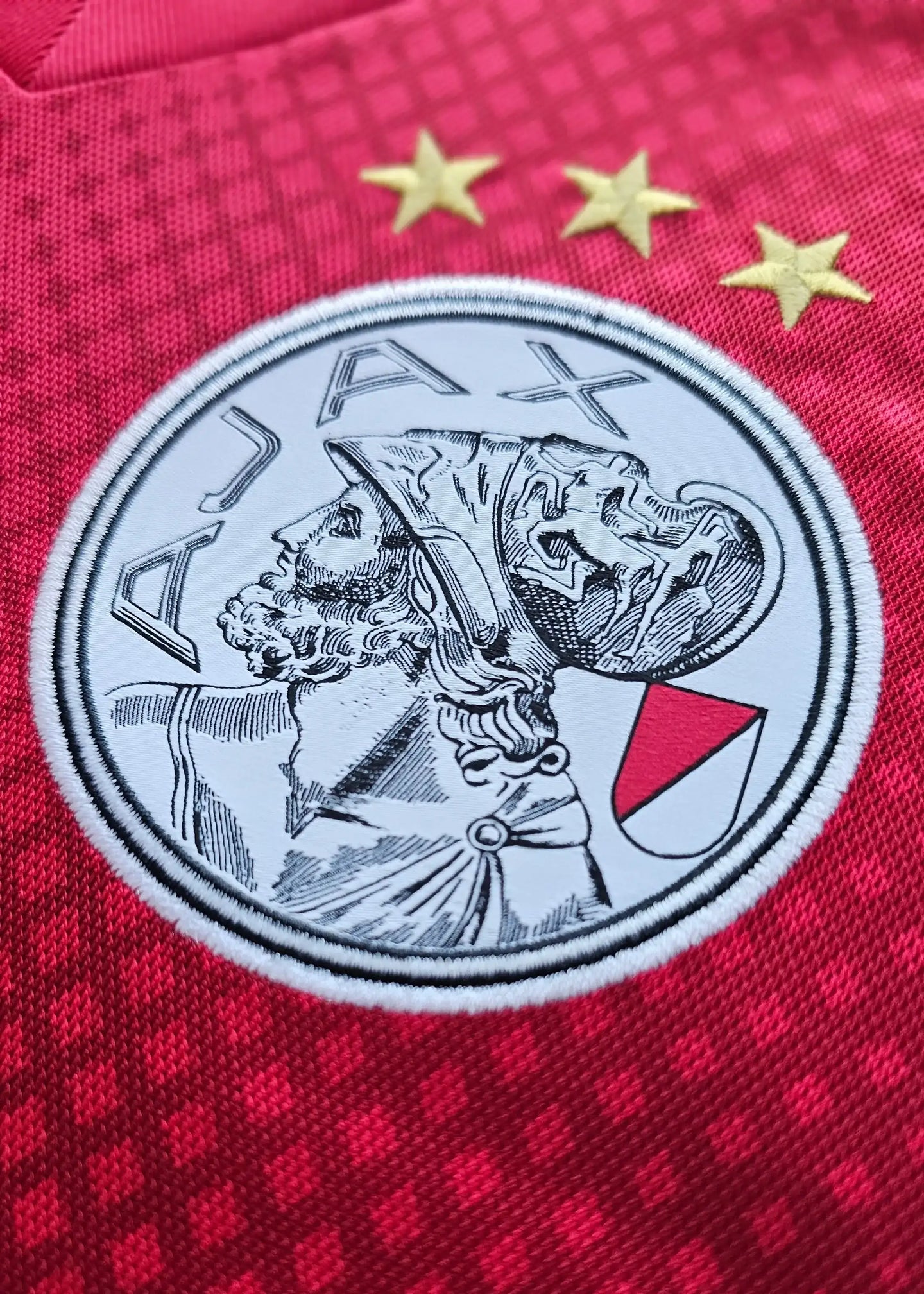 Close-up of the Ajax crest showing three gold stars and 'AJAX' on a red background.