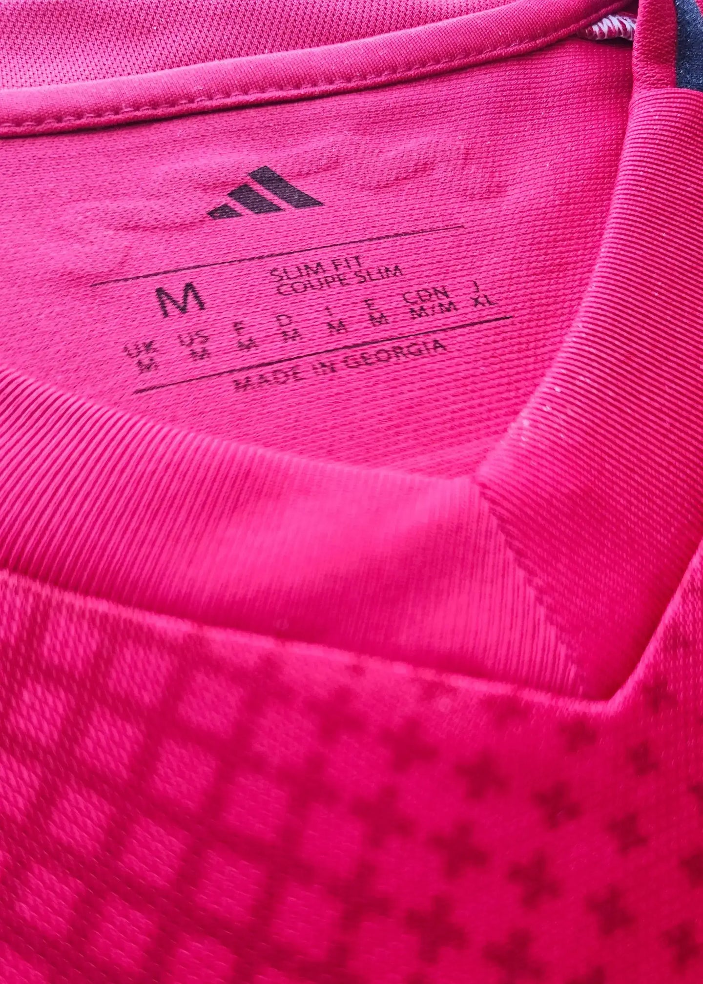 Close-up of the size label showing M, slim fit, and adidas logo on the red shirt.