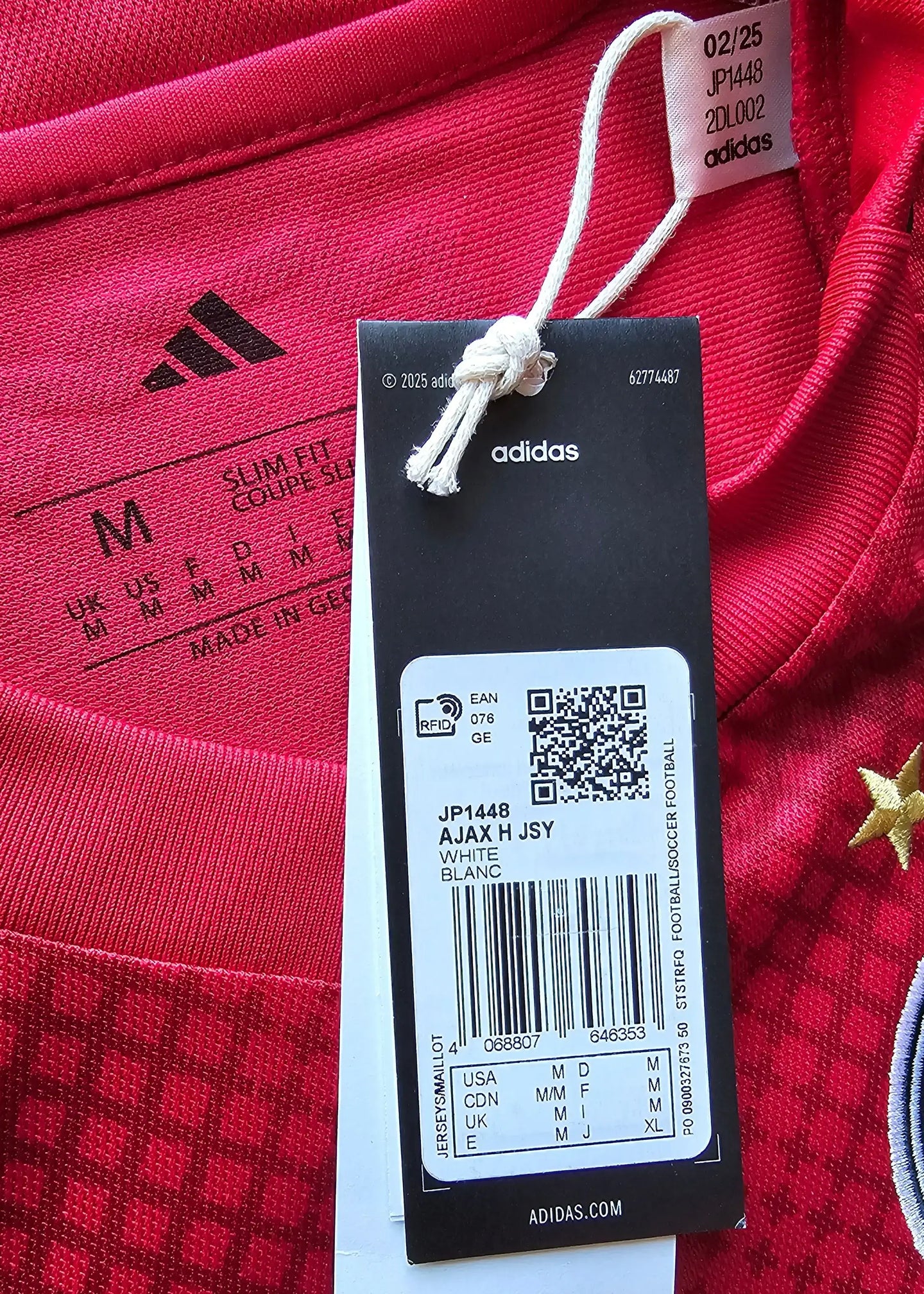 Close-up of the red Ajax shirt tag with adidas logo, size M, and care instructions, plus white tag details.