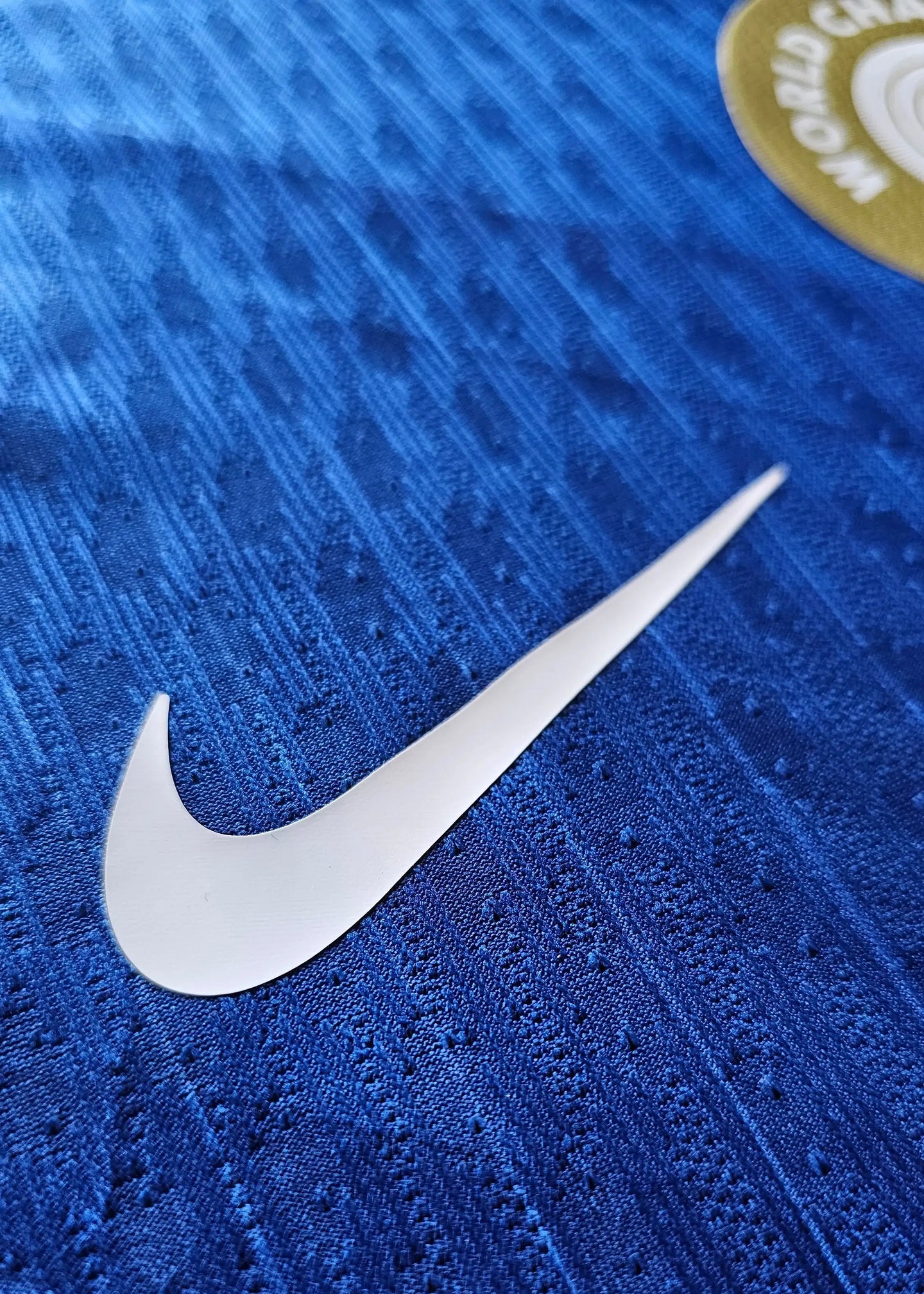 Close-up of Nike swoosh on blue Chelsea football shirt with woven texture.