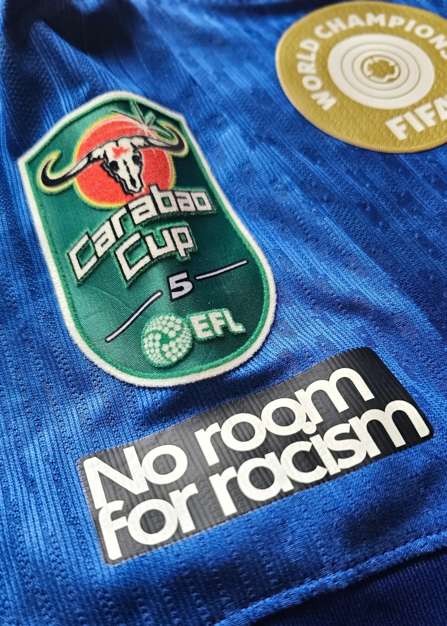 Detail view showing Carabao Cup badge and "No room for racism" text on blue football shirt.
