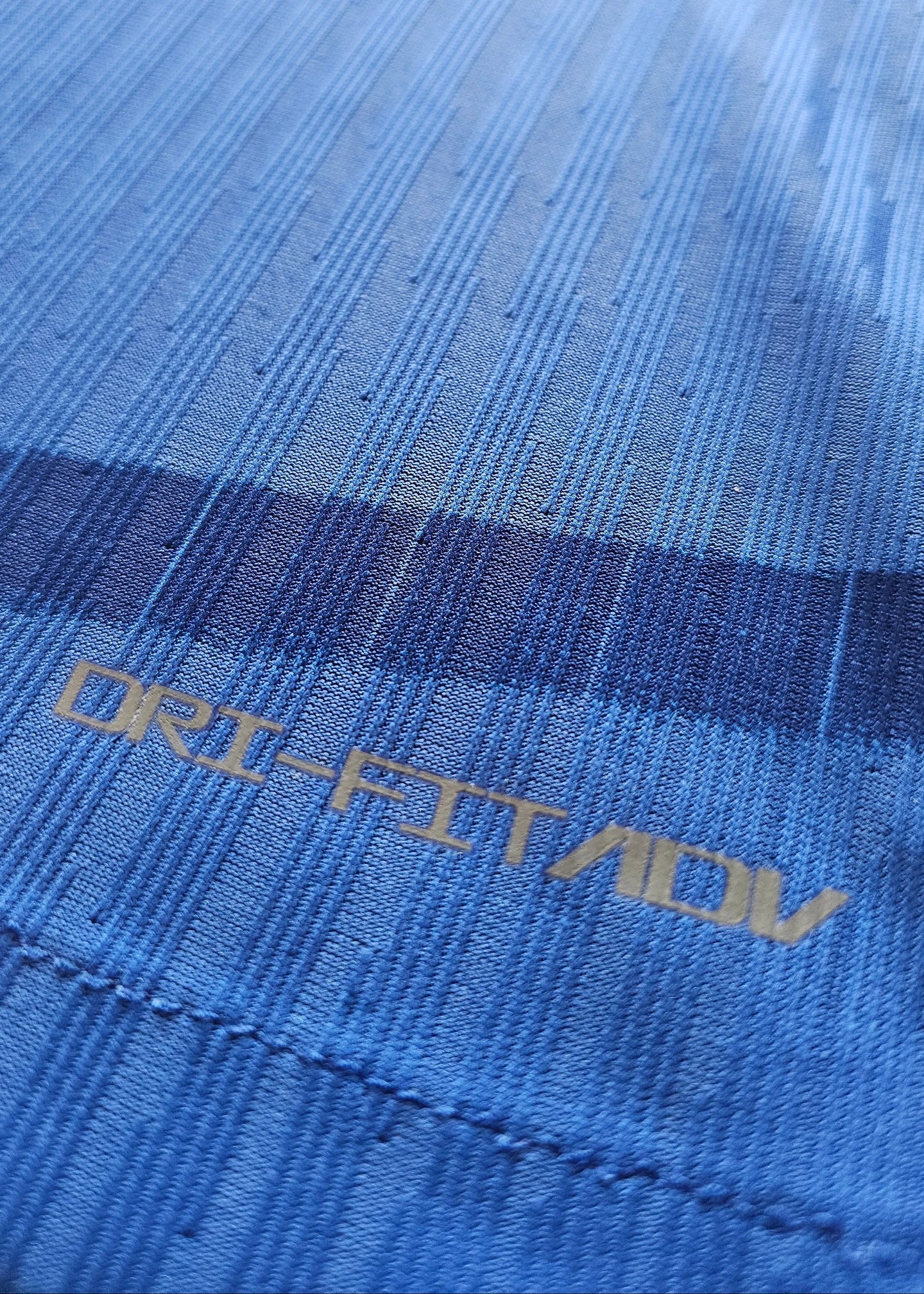 Close-up detail of the DRI-FIT ADV label on a blue football shirt.