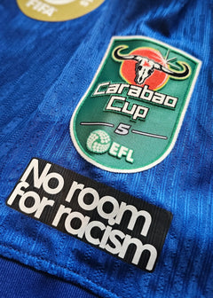 Close-up of Chelsea F.C. shirt showing Carabao Cup patch with 'No room for racism' text.