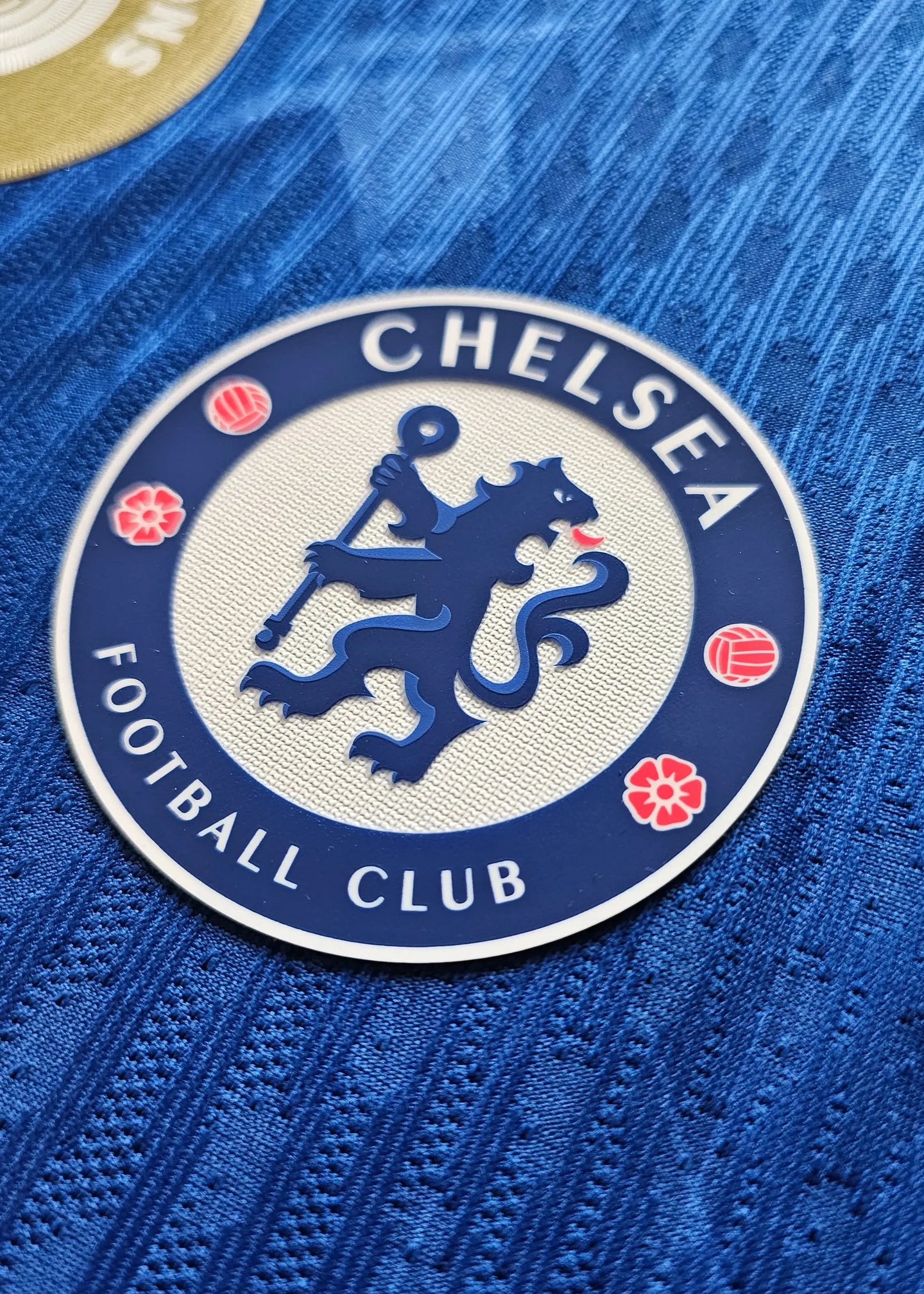 Close-up of Chelsea Football Club crest featuring a lion, red floral accents, and textured blue fabric.