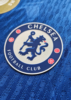 Close-up of Chelsea Football Club crest featuring a lion, red floral accents, and textured blue fabric.