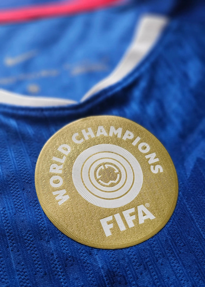 Crest detail featuring the FIFA World Champions badge on a blue football shirt.