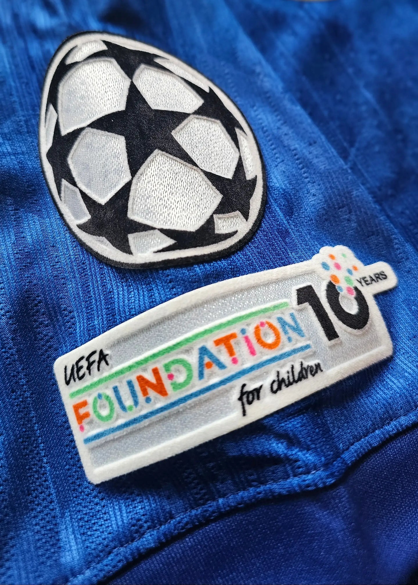 Detailed view of UEFA Champions League logo and UEFA Foundation for Children 10 Years patch on blue shirt.