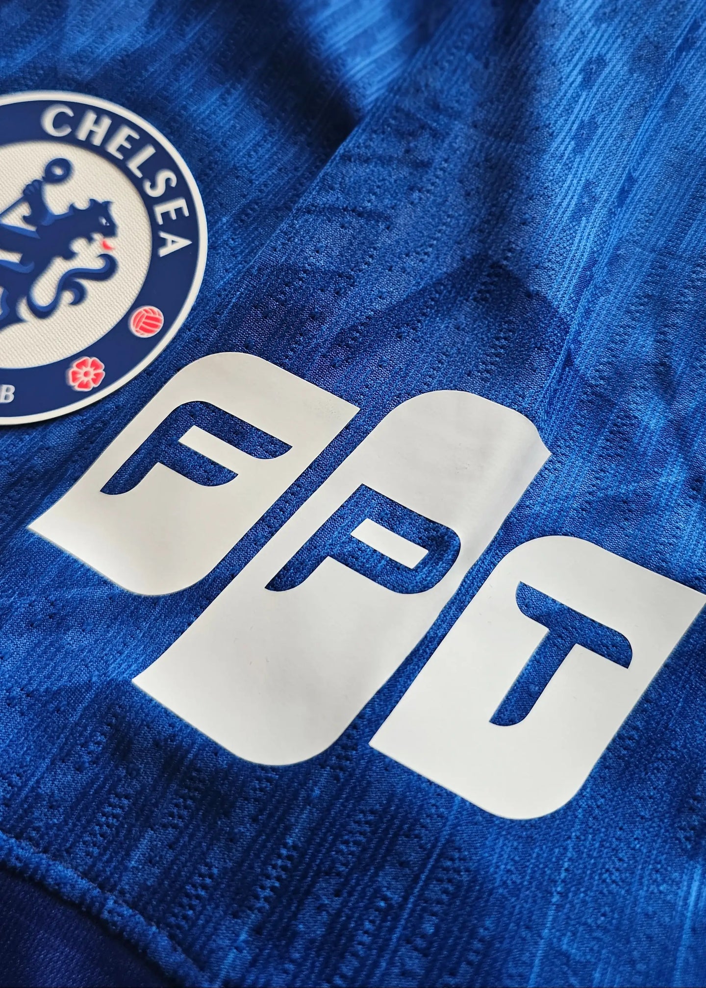 Close-up of Chelsea F.C. crest and FPT sponsor logo on a blue football shirt.
