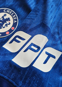 Close-up of Chelsea F.C. crest and FPT sponsor logo on a blue football shirt.