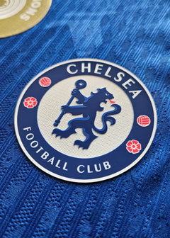 Detail of the Chelsea F.C. crest with lion and Football Club text on a blue background.