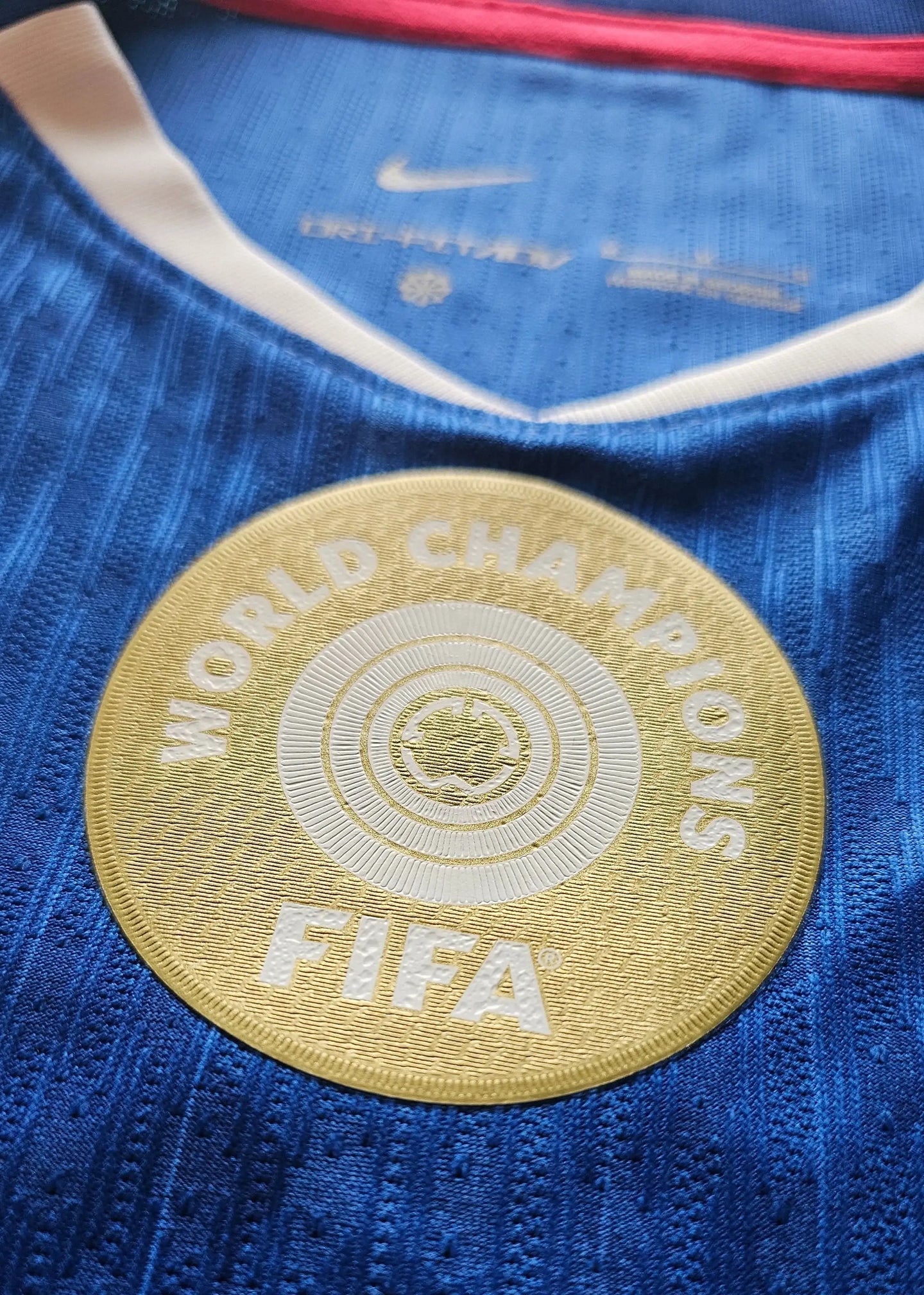 Crest detail featuring the FIFA World Champions badge on a blue football shirt.