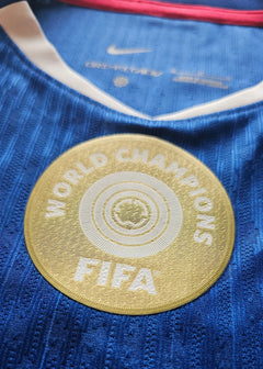 Crest detail featuring the FIFA World Champions badge on a blue football shirt.