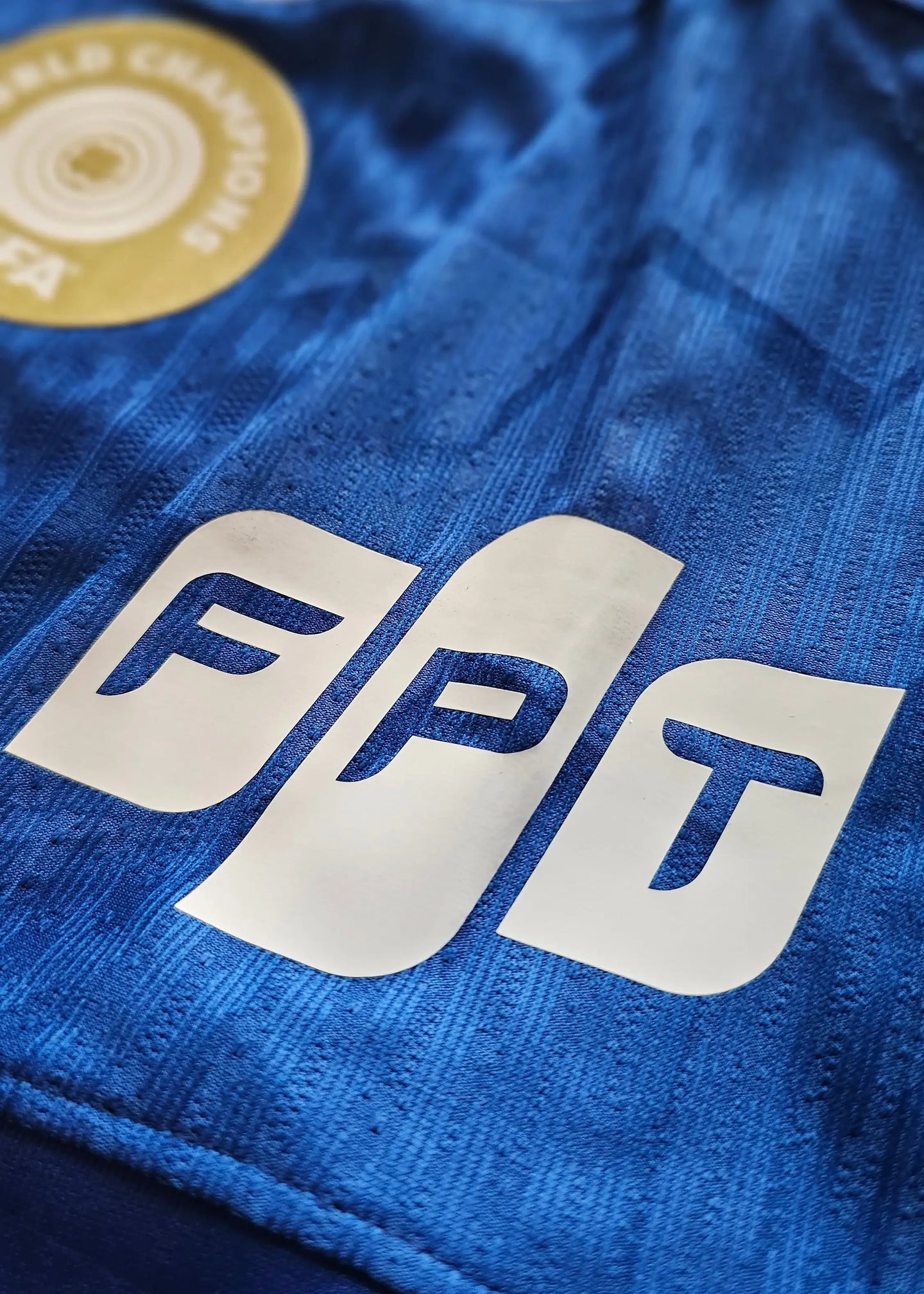 Close-up view of FPT wordmark and World Champions badge on blue football shirt.
