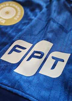 Close-up view of FPT wordmark and World Champions badge on blue football shirt.