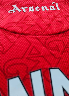 Close-up view showing Arsenal text in white on a red football shirt fabric.