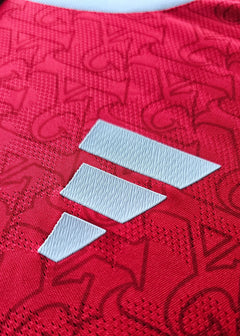 Close-up of red football shirt fabric featuring three white adidas stripes.