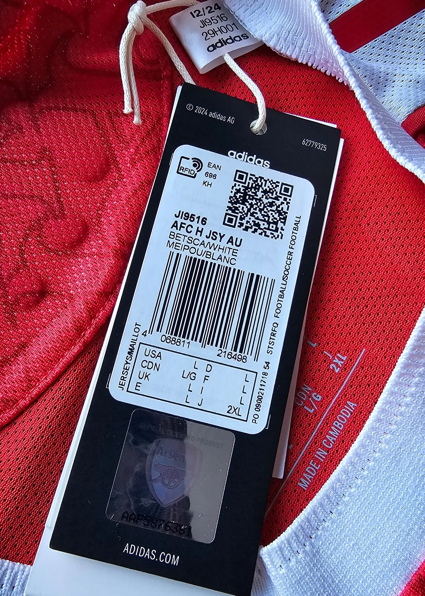 Label showing size and barcode on a red football shirt with white trim, featuring an adidas tag.