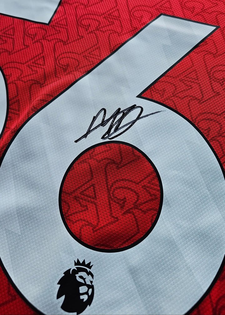 Close-up of No. 56 with visible signature on red Arsenal football shirt and league badge.