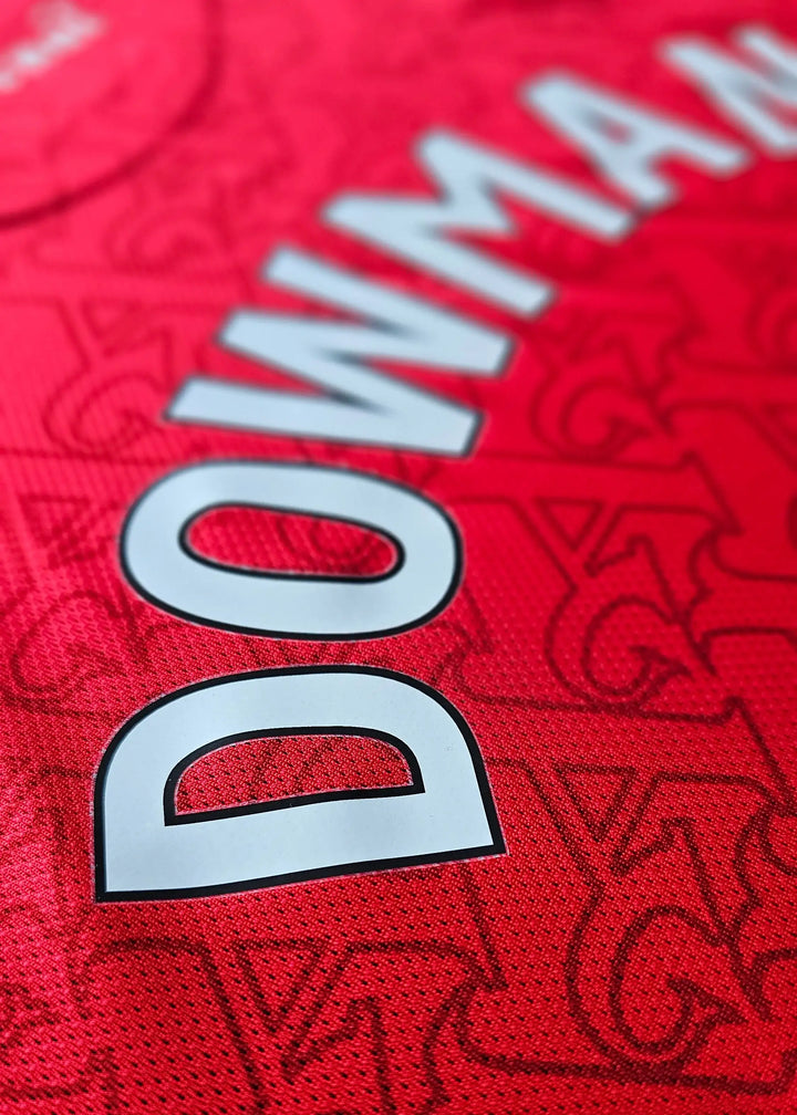 Close-up of the name DOWMAN on a red Arsenal football shirt with intricate background pattern.