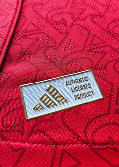 Detail showing adidas logo with text 'AUTHENTIC LICENSED PRODUCT' on red fabric background.