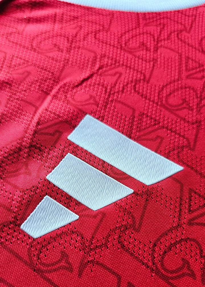 Close-up detail of the red textured fabric and white adidas logo on an Arsenal football shirt.